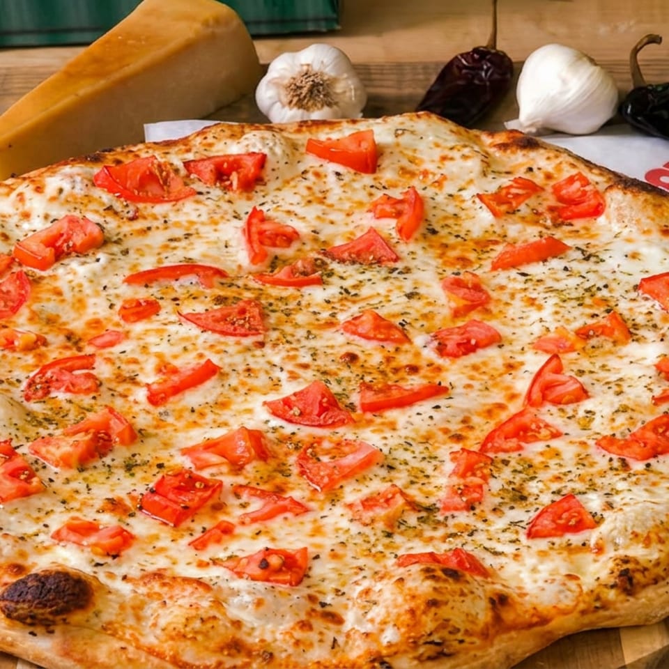 Large cheesy pizza topped with chopped tomatoes and herbs on a wooden board, surrounded by garlic, peppers, and cheese.